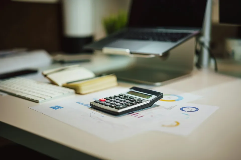 A calculator on a desk beside printed charts and a laptop