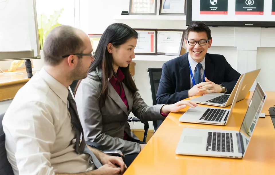 A consultant in a suit going through a case with two colleagues at their laptops